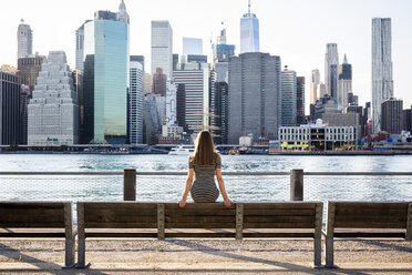 USA, New York, Brooklyn, Rückenansicht einer Frau, die auf einer Bank vor dem East River und der Skyline von Manhattan sitzt - GIOF04571