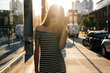 USA, New York, Brooklyn, Dumbo, junge Frau in gestreiftem Kleid und Sonnenbrille bei Sonnenuntergang - GIOF04590