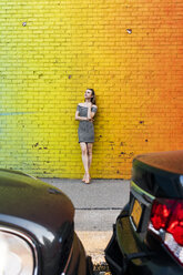 USA, New York, Brooklyn, Dumbo, young woman wearing striped dress leaning against yellow wall - GIOF04594