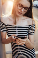 Woman listening music with smartphone and earphones at sunset - GIOF04598