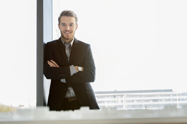 Young businessman in front of office window looking down at architectural model - CUF44315