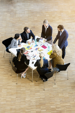 Geschäftsfrauen und -männer im Atrium eines Büros, die Designmuster auf einem Tisch diskutieren, Blickwinkel, lizenzfreies Stockfoto