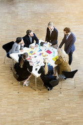 Geschäftsfrauen und -männer im Atrium eines Büros, die Designmuster auf einem Tisch diskutieren, Blickwinkel - CUF44320