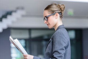 Businesswoman reading newspaper in office - CUF44335