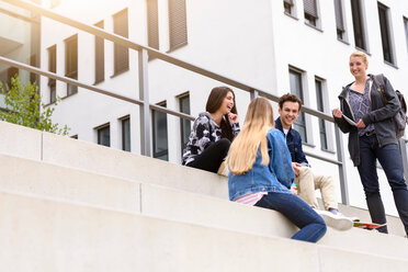 Vier junge erwachsene Studenten sitzen plaudernd auf einer Treppe vor dem College, Blick aus geringer Höhe - CUF44343