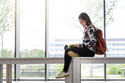 Studentin sitzt auf einem Tisch und liest ein Buch im Foyer der Universität - CUF44352