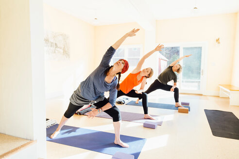 Drei Frauen üben im Yogastudio die Yogapose des verlängerten seitlichen Ausfallschrittes (Parsvakonasana) - CUF44384