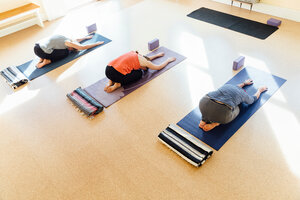 Drei Frauen üben Balasana (Kinderstellung) im Yogastudio - CUF44385