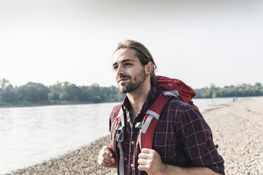 Selbstbewusster junger Mann mit Rucksack am Flussufer - UUF15310