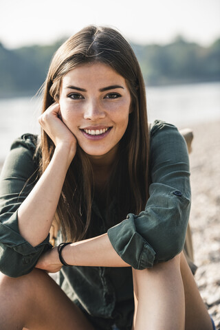 Porträt einer lächelnden jungen Frau, die im Freien sitzt, lizenzfreies Stockfoto