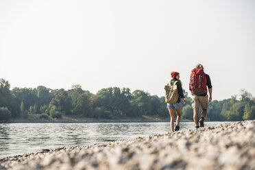 Rückansicht eines jungen Paares mit Rucksäcken beim Spaziergang am Flussufer - UUF15323