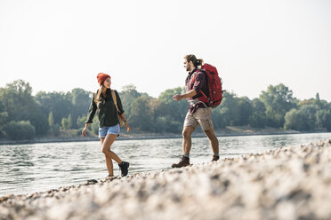 Young couple with backpacks walking at the riverside - UUF15324