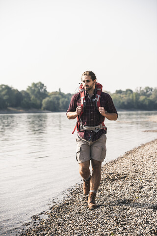 Junger Mann mit Rucksack beim Spaziergang am Flussufer, lizenzfreies Stockfoto