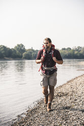 Junger Mann mit Rucksack beim Spaziergang am Flussufer - UUF15330