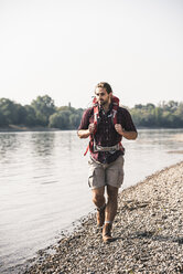 Young man with backpack walking at the riverside - UUF15330