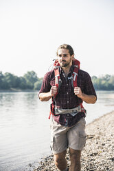 Young man with backpack walking at the riverside - UUF15331