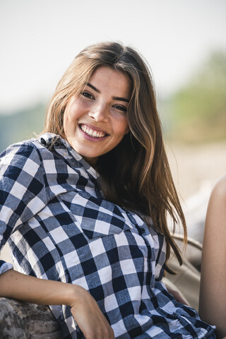 Porträt einer lächelnden jungen Frau, die im Freien sitzt, lizenzfreies Stockfoto