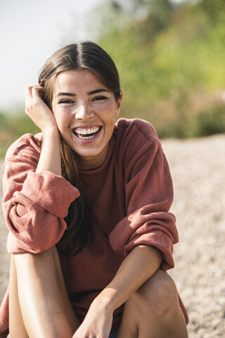 Porträt einer lachenden jungen Frau, die im Freien sitzt, lizenzfreies Stockfoto