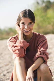 Porträt einer lächelnden jungen Frau, die im Freien sitzt - UUF15347