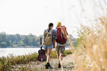 Rückansicht eines jungen Paares mit Rucksäcken und Gitarre beim Spaziergang am Flussufer - UUF15361