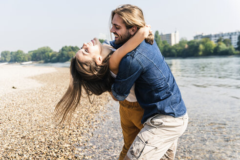 Glückliches, verliebtes junges Paar, das sich am Flussufer umarmt - UUF15366