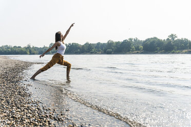 Junge Frau steht im Wasser eines Flusses und übt Yoga - UUF15374