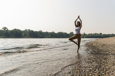 Junge Frau steht im Wasser eines Flusses und übt Yoga - UUF15375