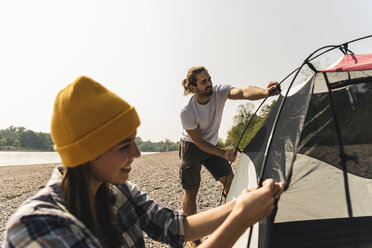 Lächelndes junges Paar beim Aufbau eines Zeltes am Flussufer - UUF15390