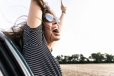 Carefree young woman leaning out of car window screaming - UUF15411