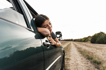Young woman leaning out of car window on dirt track - UUF15412