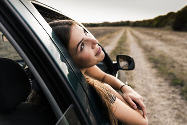 Smiling young woman leaning out of car window - UUF15413