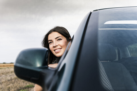 Lächelnde junge Frau lehnt sich aus dem Autofenster, lizenzfreies Stockfoto