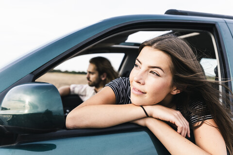 Lächelnde junge Frau lehnt sich aus dem Autofenster, lizenzfreies Stockfoto