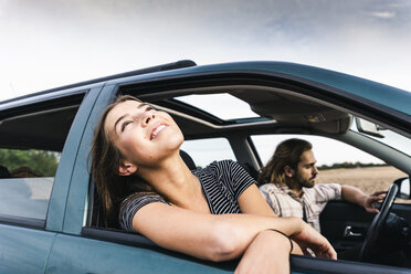 Smiling young woman leaning out of car window - UUF15417
