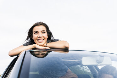 Lächelnde junge Frau schaut aus dem Schiebedach eines Autos - UUF15418