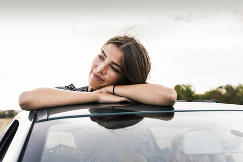 Smiling young woman looking out of sunroof of a car stock photo