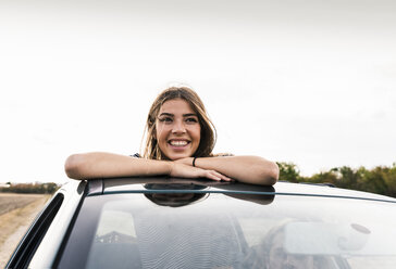 Smiling young woman looking out of sunroof of a car - UUF15423