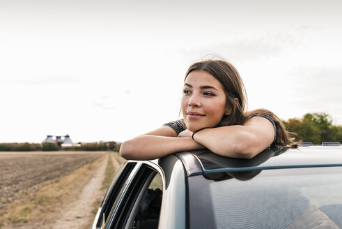 Lächelnde junge Frau schaut aus dem Schiebedach eines Autos - UUF15424