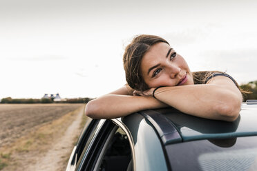 Lächelnde junge Frau schaut aus dem Schiebedach eines Autos - UUF15425