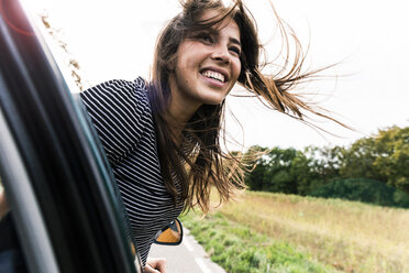 Happy young woman leaning out of car window - UUF15438