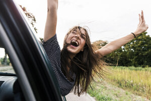 Carefree young woman leaning out of car window screaming - UUF15440