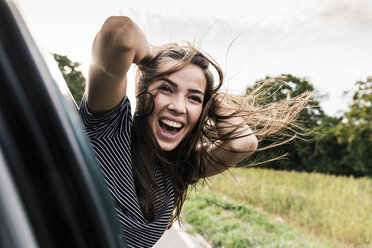 Carefree young woman leaning out of car window - UUF15441