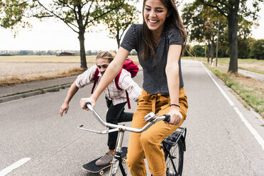 Happy young couple with bicycle and skateboard on country road - UUF15443