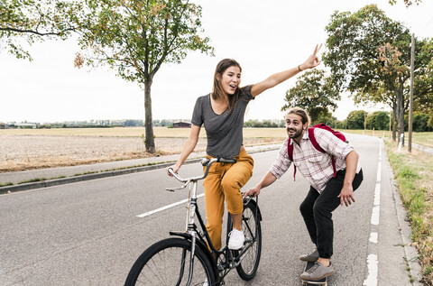 Glückliches junges Paar mit Fahrrad und Skateboard auf der Landstraße, lizenzfreies Stockfoto