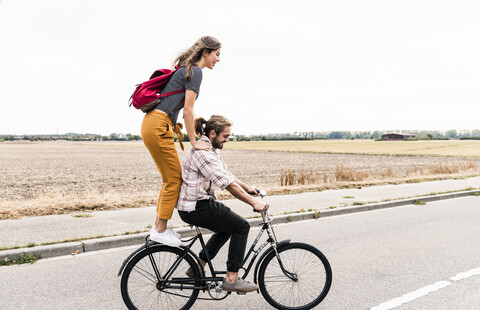 Happy young couple riding together on one bicycle on country road stock photo