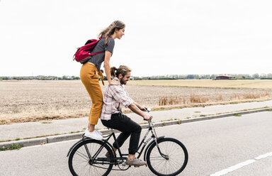 Glückliches junges Paar fährt zusammen auf einem Fahrrad auf einer Landstraße - UUF15445