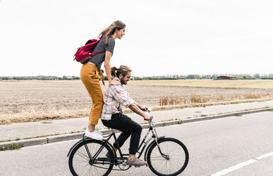 Happy young couple riding together on one bicycle on country road - UUF15445