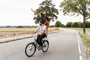 Glückliches junges Paar fährt zusammen auf einem Fahrrad auf einer Landstraße - UUF15446