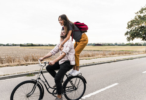 Glückliches junges Paar fährt zusammen auf einem Fahrrad auf einer Landstraße, lizenzfreies Stockfoto