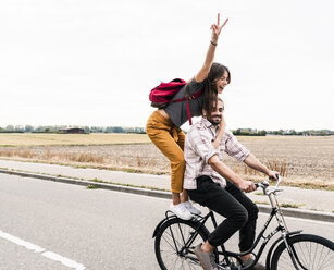 Glückliches junges Paar fährt zusammen auf einem Fahrrad auf einer Landstraße - UUF15448